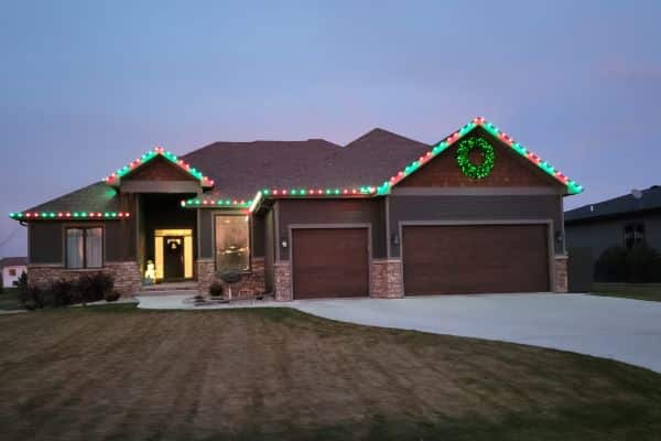 Home with colorful roofline lights and a wreath above the garage doors.