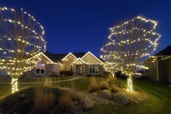 House with lights along the roofline and on nearby trees at dusk.